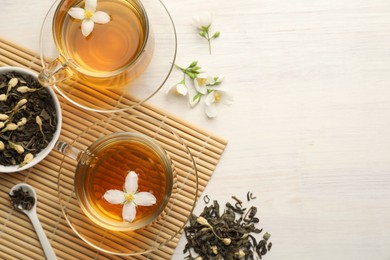 Photo of Tasty jasmine tea in cups, dry leaves and flowers on white wooden table, flat lay. Space for text