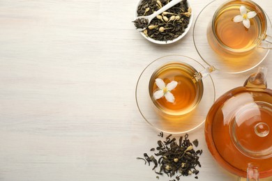 Photo of Tasty jasmine tea in cups, teapot, dry leaves and flowers on white wooden table, flat lay. Space for text