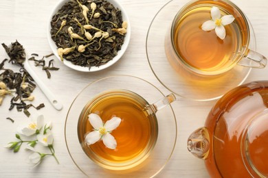Photo of Tasty jasmine tea in cups, teapot, dry leaves and flowers on white wooden table, flat lay