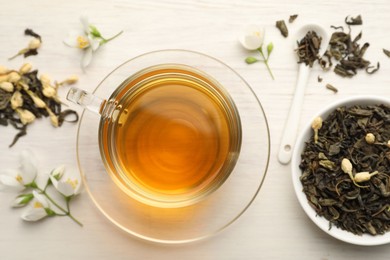 Photo of Tasty jasmine tea in cup, dry leaves and flowers on white wooden table, flat lay