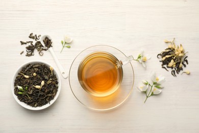 Photo of Tasty jasmine tea in cup, dry leaves and flowers on white wooden table, flat lay