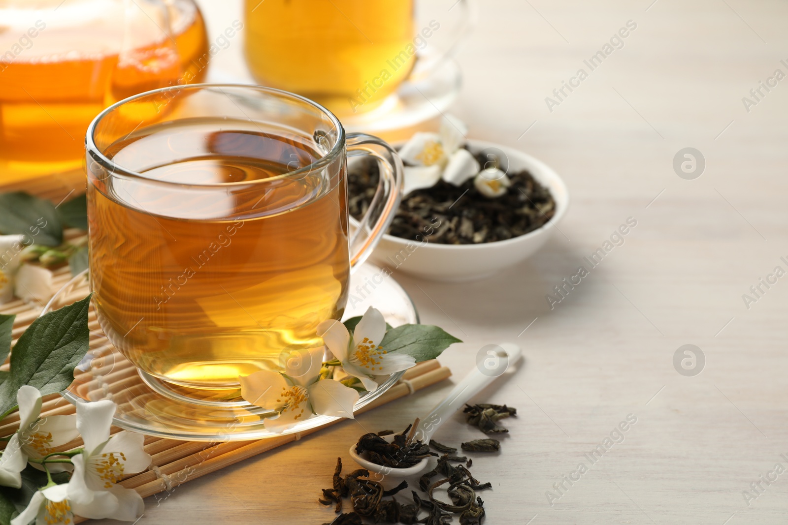 Tasty jasmine tea in cup, dry leaves and flowers on white wooden table, closeup. Space for text Photo of Tasty jasmine tea in cup, dry leaves and flowers on white wooden table, closeup. Space for text