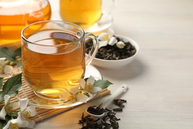 Photo of Tasty jasmine tea in cup, dry leaves and flowers on white wooden table, closeup. Space for text
