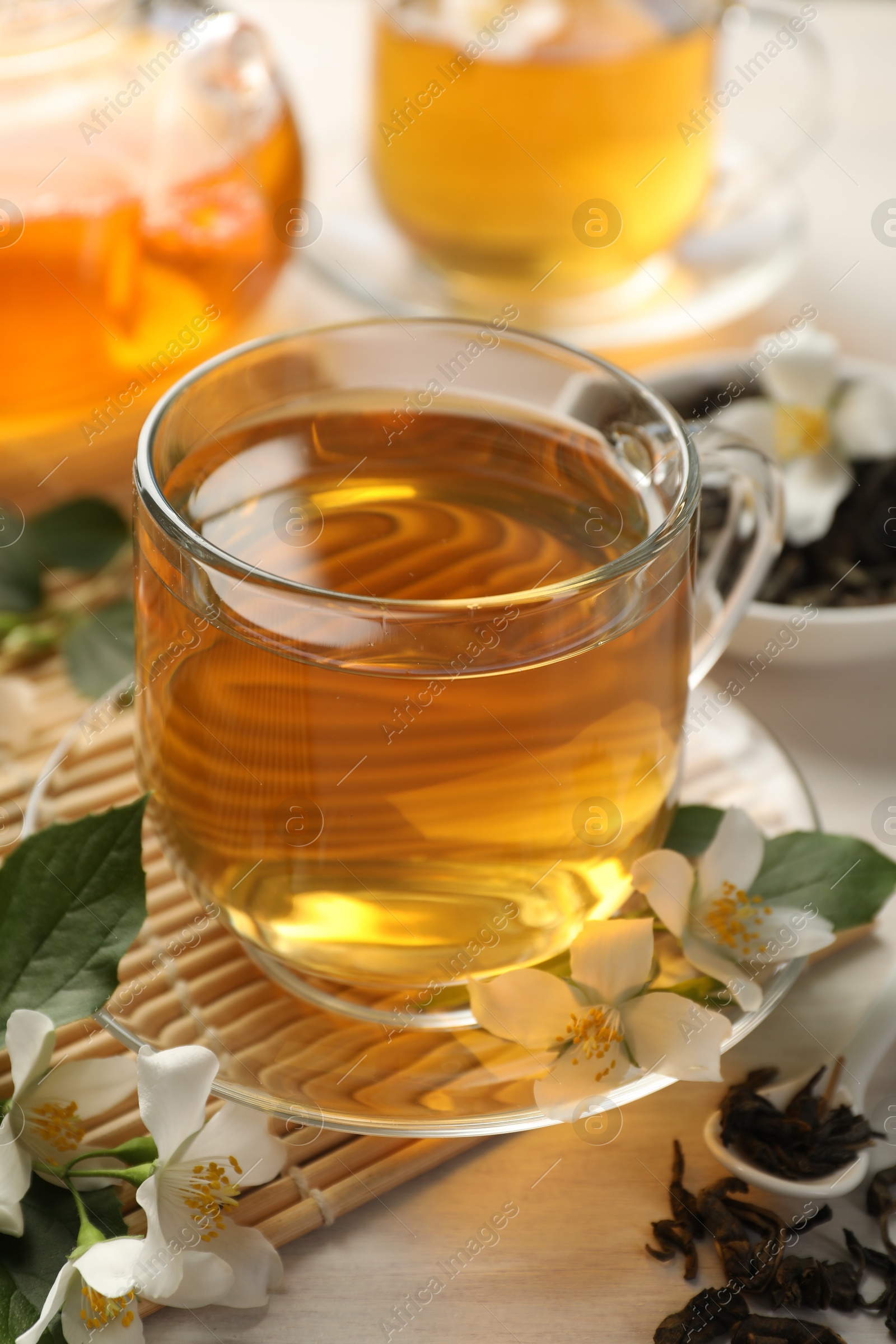 Tasty jasmine tea in cup, dry leaves and flowers on white wooden table, closeup Photo of Tasty jasmine tea in cup, dry leaves and flowers on white wooden table, closeup
