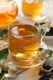 Photo of Tasty jasmine tea in cup, dry leaves and flowers on white wooden table, closeup