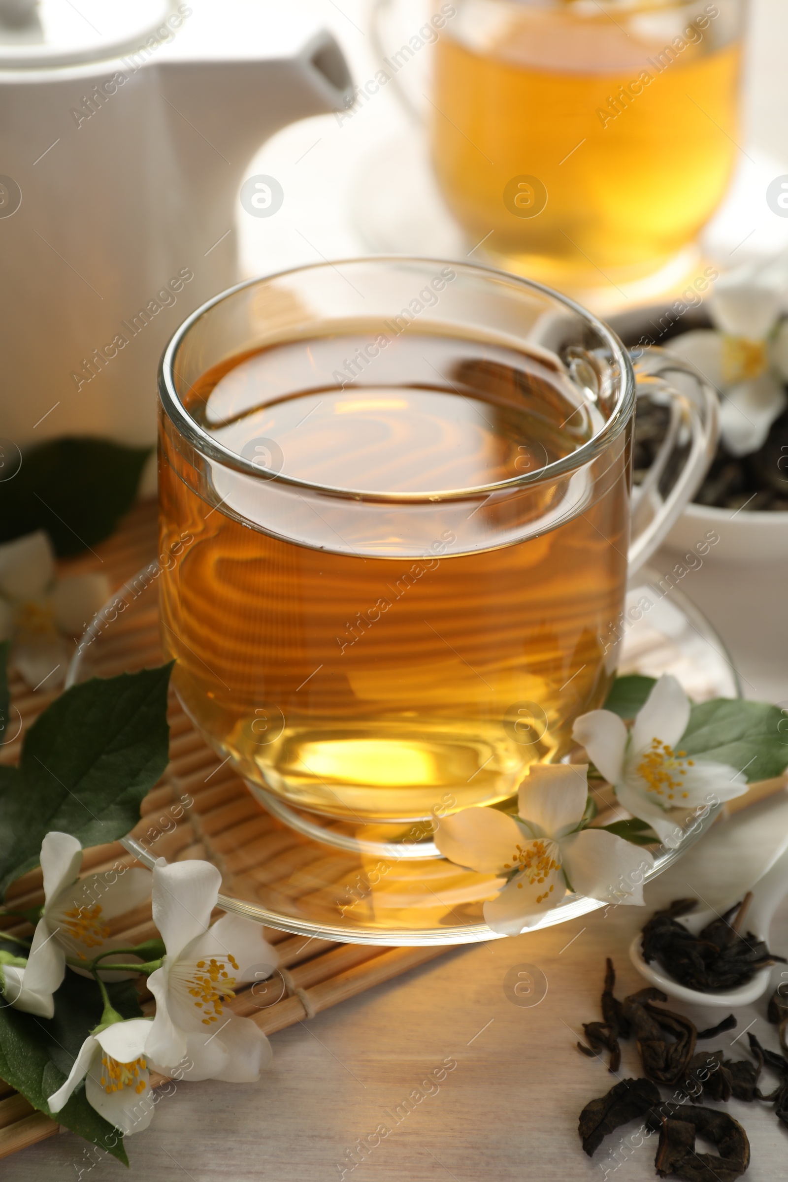 Tasty jasmine tea in cup, dry leaves and flowers on white wooden table, closeup Photo of Tasty jasmine tea in cup, dry leaves and flowers on white wooden table, closeup