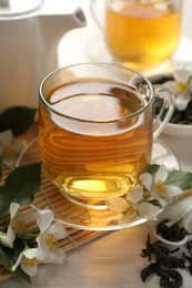 Photo of Tasty jasmine tea in cup, dry leaves and flowers on white wooden table, closeup