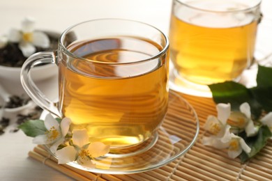 Photo of Tasty jasmine tea in cups, dry leaves and flowers on white wooden table, closeup