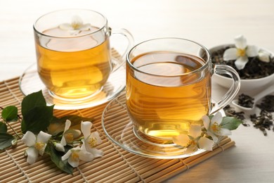Photo of Tasty jasmine tea in cups, dry leaves and flowers on white wooden table, closeup