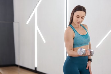 Photo of Woman exercising with dumbbell in fitness studio, space for text