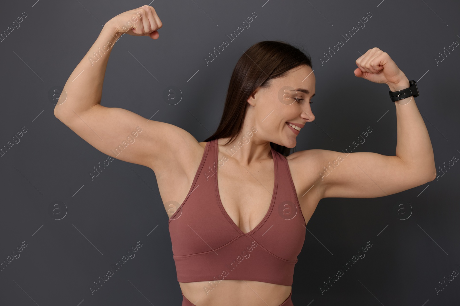 Woman in fitness clothes showing her biceps on grey background Photo of Woman in fitness clothes showing her biceps on grey background