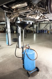 Photo of Dirty old motor oil dripping from car engine into container in workshop