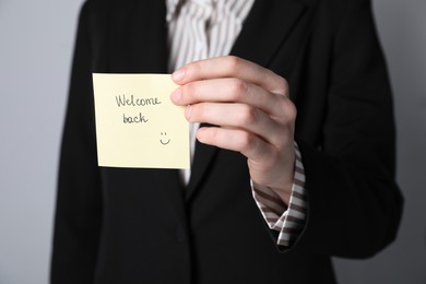 Photo of Businesswoman holding sticky note with word Welcome Back on grey background, closeup