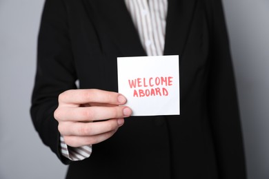 Photo of Human resources manager holding sticky note with words Welcome Aboard on grey background, closeup