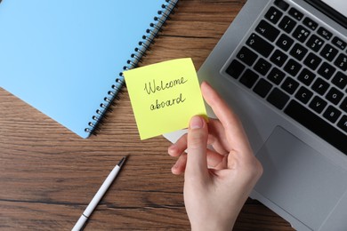 Photo of Woman holding paper note with words Welcome Aboard at wooden table, top view