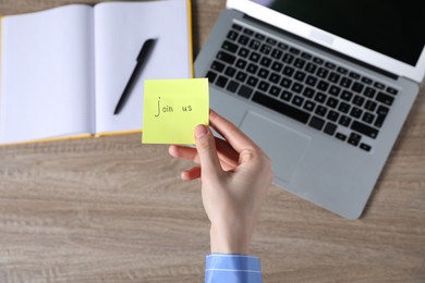 Photo of Woman holding paper note with words Join Us at wooden table, top view