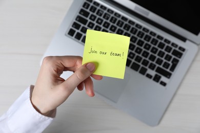 Photo of Woman holding paper note with words Join Our Team at light table, top view