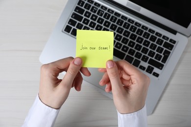 Photo of Woman holding paper note with words Join Our Team at light wooden table, top view