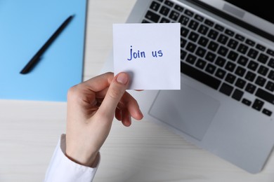 Photo of Woman holding paper note with words Join Us at light wooden table, top view