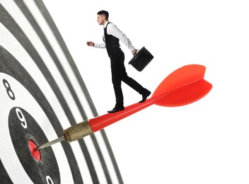 Image of Concepts of targeting, decision and goal achievement. Businessman walking on dart sticking in center of dartboard against white background