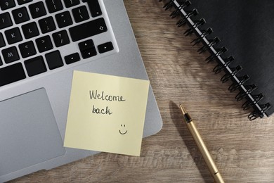 Photo of Paper note with words Welcome Back, pen and notepad on wooden table, flat lay