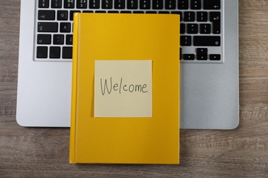 Photo of Sticky note with word Welcome, notebook and laptop on wooden table, top view