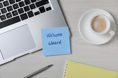 Photo of Paper note with word Welcome Aboard, laptop, cup of coffee and pen on light wooden table, flat lay