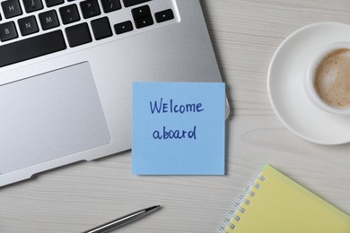 Photo of Paper note with word Welcome Aboard, laptop, cup of coffee and pen on light wooden table, flat lay