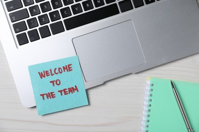 Photo of Paper note with words Welcome To The Team, laptop, notepad and pen on light wooden table, flat lay
