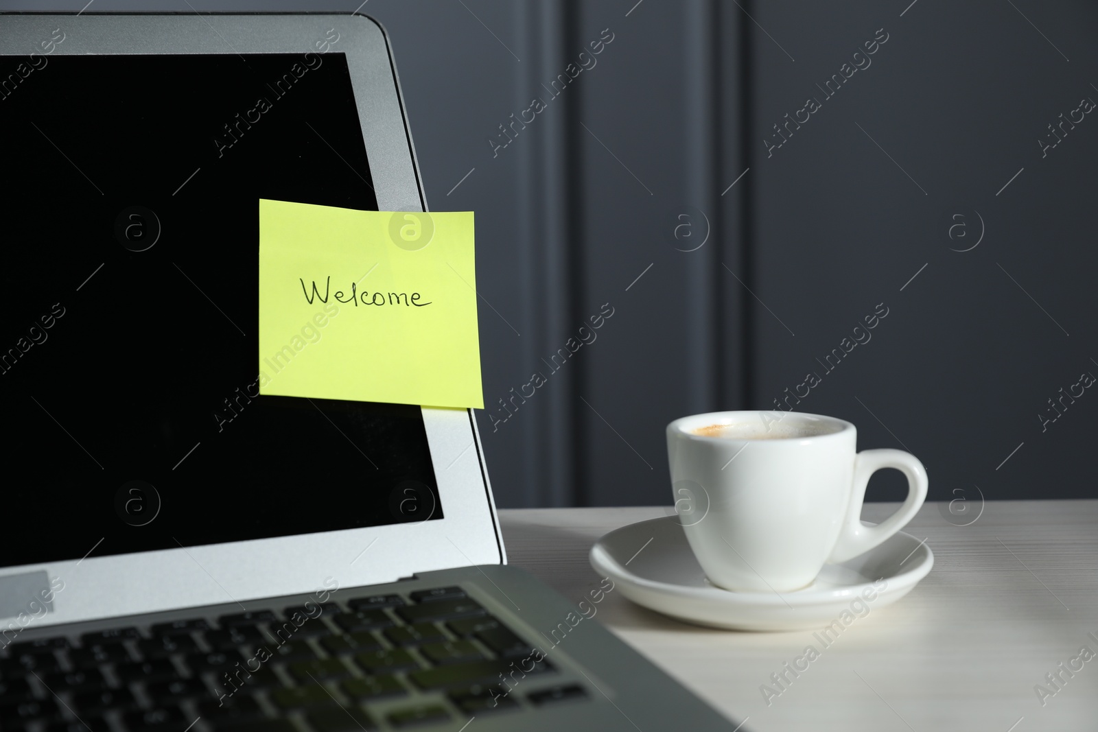 Sticky note with word Welcome, laptop and cup on white wooden table against grey background, closeup Photo of Sticky note with word Welcome, laptop and cup on white wooden table against grey background, closeup