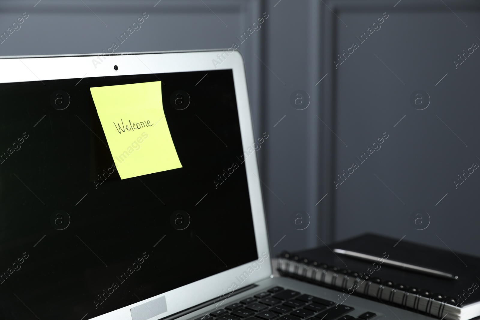 Sticky note with word Welcome, laptop and notepad on table against grey background, closeup Photo of Sticky note with word Welcome, laptop and notepad on table against grey background, closeup
