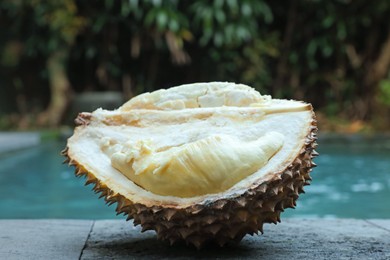 Photo of Fresh ripe durian on stone surface near swimming pool outdoors, closeup