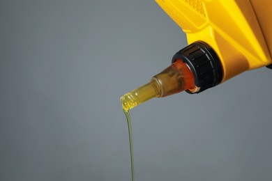 Photo of Pouring motor oil from yellow canister on grey background, closeup. Space for text