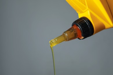 Photo of Pouring motor oil from yellow canister on grey background, closeup. Space for text