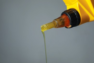 Photo of Pouring motor oil from yellow canister on grey background, closeup. Space for text