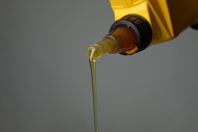 Photo of Pouring motor oil from yellow canister on grey background, closeup. Space for text