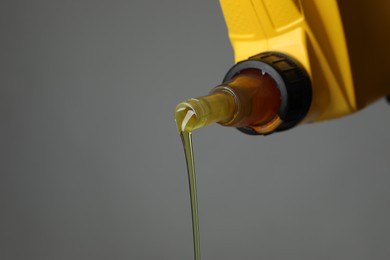 Photo of Pouring motor oil from yellow canister on grey background, closeup. Space for text