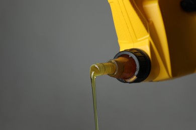 Photo of Pouring motor oil from yellow canister on grey background, closeup. Space for text