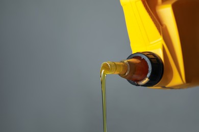 Photo of Pouring motor oil from yellow canister on grey background, closeup. Space for text