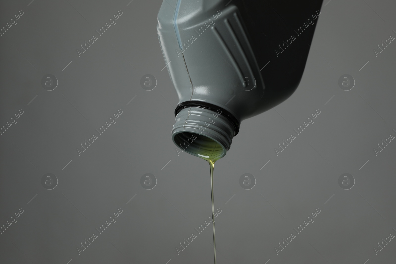 Pouring motor oil from canister on grey background, closeup. Space for text Photo of Pouring motor oil from canister on grey background, closeup. Space for text