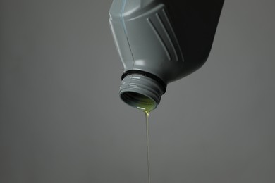 Photo of Pouring motor oil from canister on grey background, closeup. Space for text