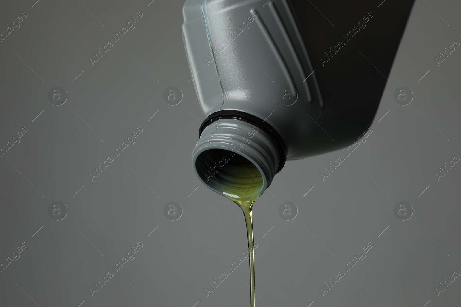 Pouring motor oil from canister on grey background, closeup. Space for text Photo of Pouring motor oil from canister on grey background, closeup. Space for text