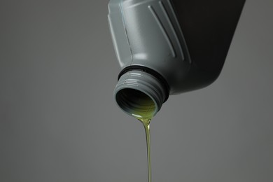 Photo of Pouring motor oil from canister on grey background, closeup. Space for text