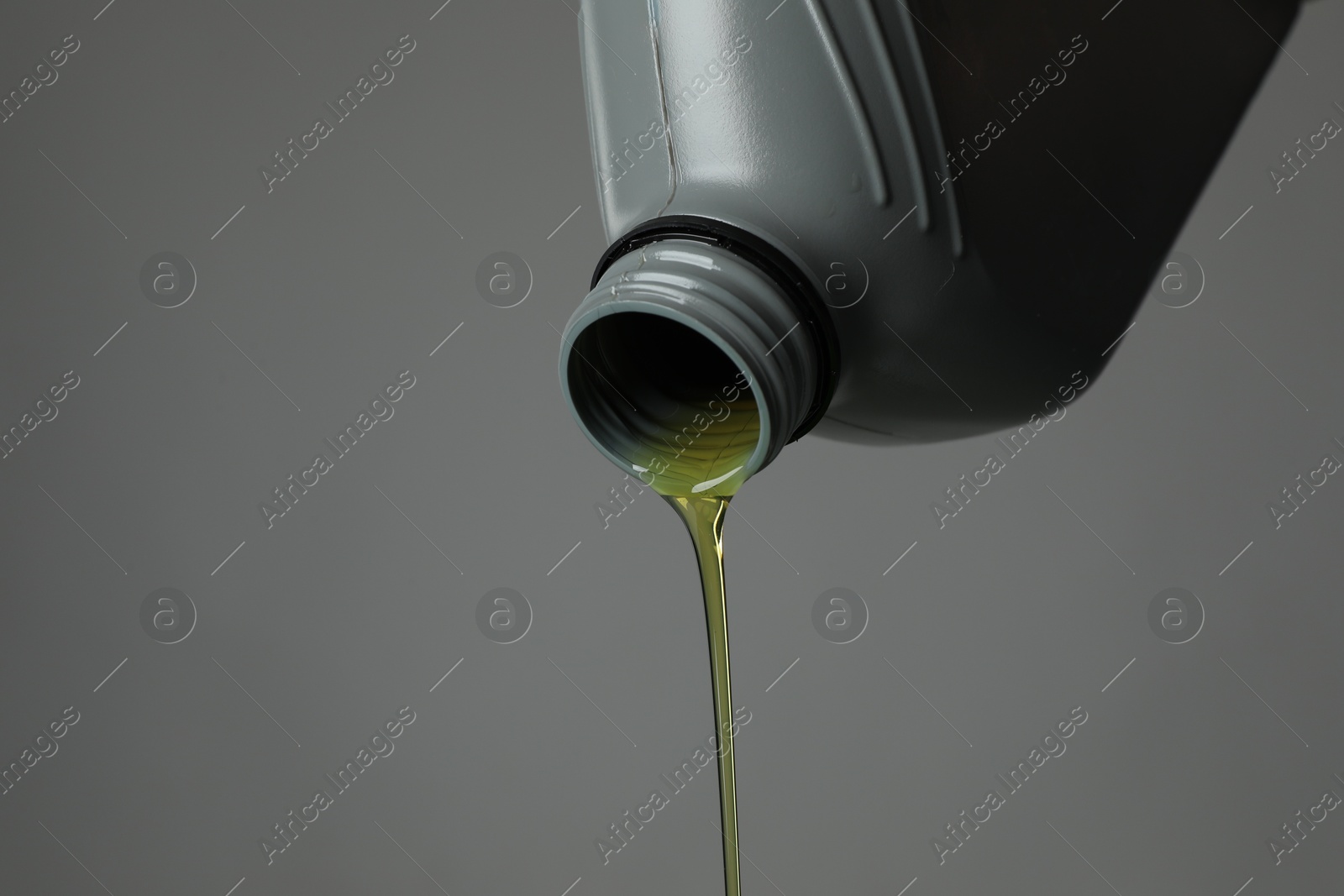 Pouring motor oil from canister on grey background, closeup. Space for text Photo of Pouring motor oil from canister on grey background, closeup. Space for text