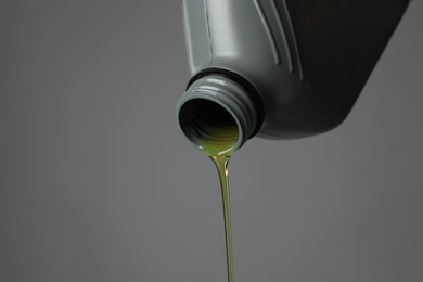 Photo of Pouring motor oil from canister on grey background, closeup. Space for text