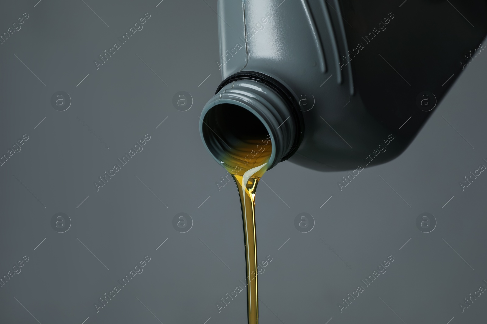 Pouring motor oil from canister on grey background, closeup. Space for text Photo of Pouring motor oil from canister on grey background, closeup. Space for text