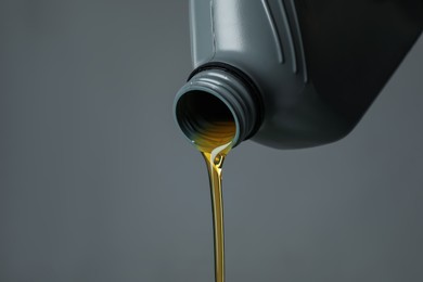 Photo of Pouring motor oil from canister on grey background, closeup. Space for text