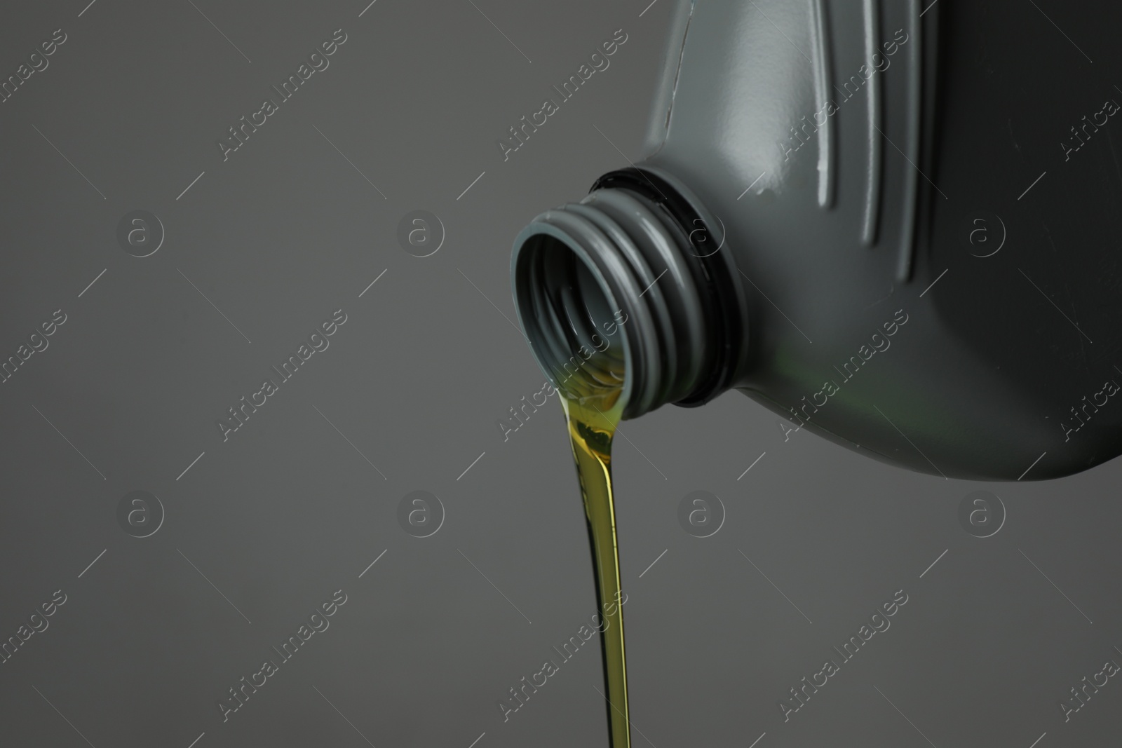 Pouring motor oil from canister on grey background, closeup. Space for text Photo of Pouring motor oil from canister on grey background, closeup. Space for text