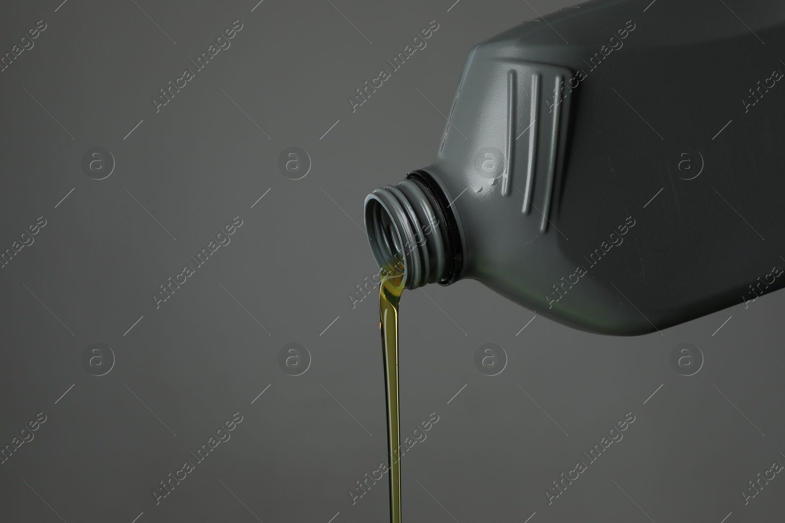 Pouring motor oil from canister on grey background, closeup. Space for text Photo of Pouring motor oil from canister on grey background, closeup. Space for text