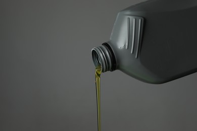 Photo of Pouring motor oil from canister on grey background, closeup. Space for text